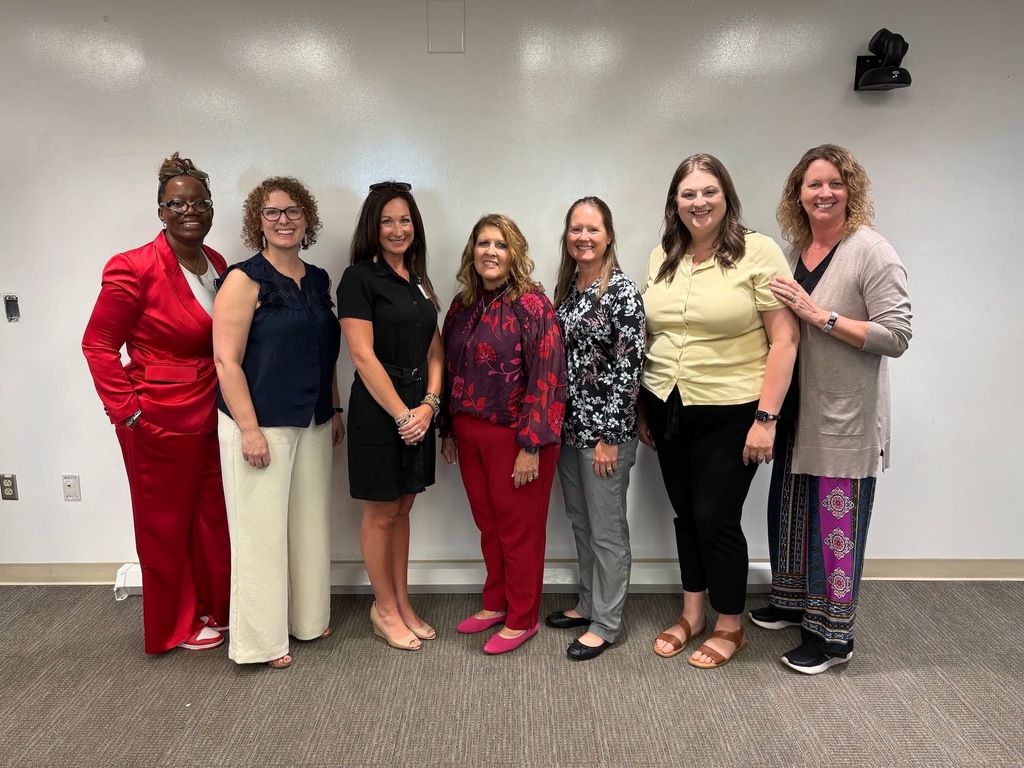 There are seven women posed for a group picture. 