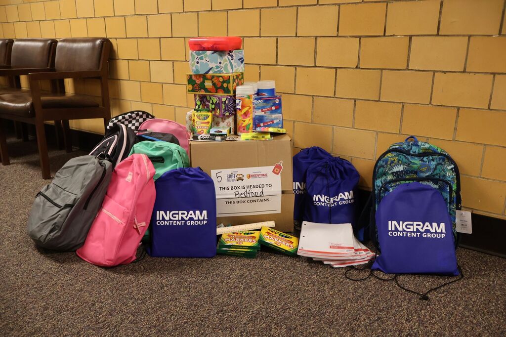 This is a photo of a box with school supplies such as backpacks, tissues, markers and papers sitting on it and around it. 