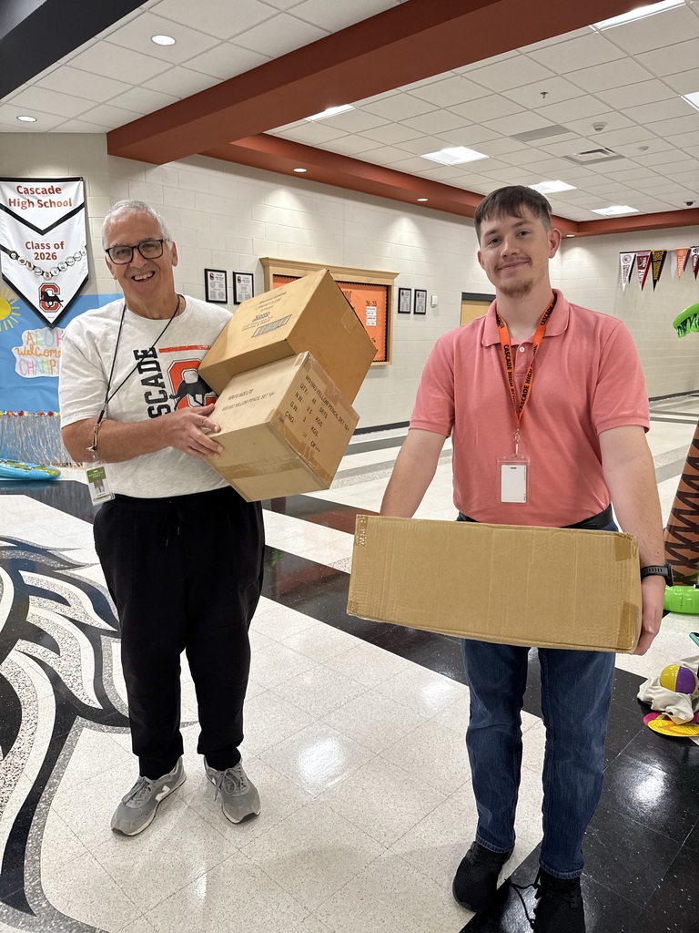 Two staff members holding donation boxes in Cascade High School hallway during Musgrave Pencil Company pencil donation event.