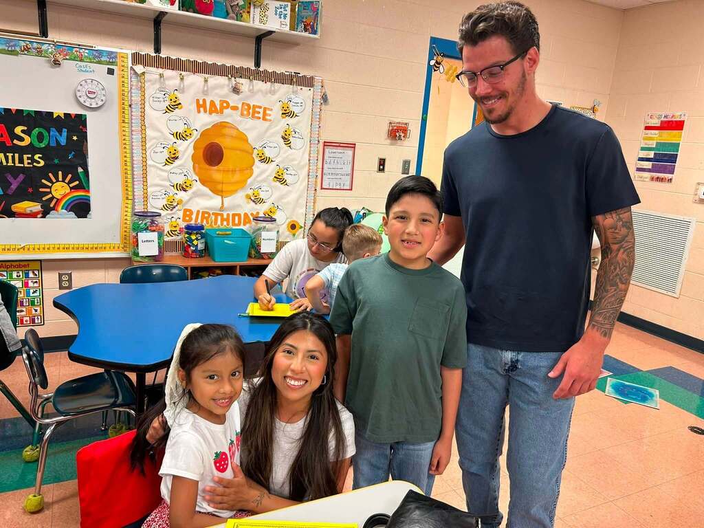 There are four people in this picture who are all posed for a group picture in a classroom.