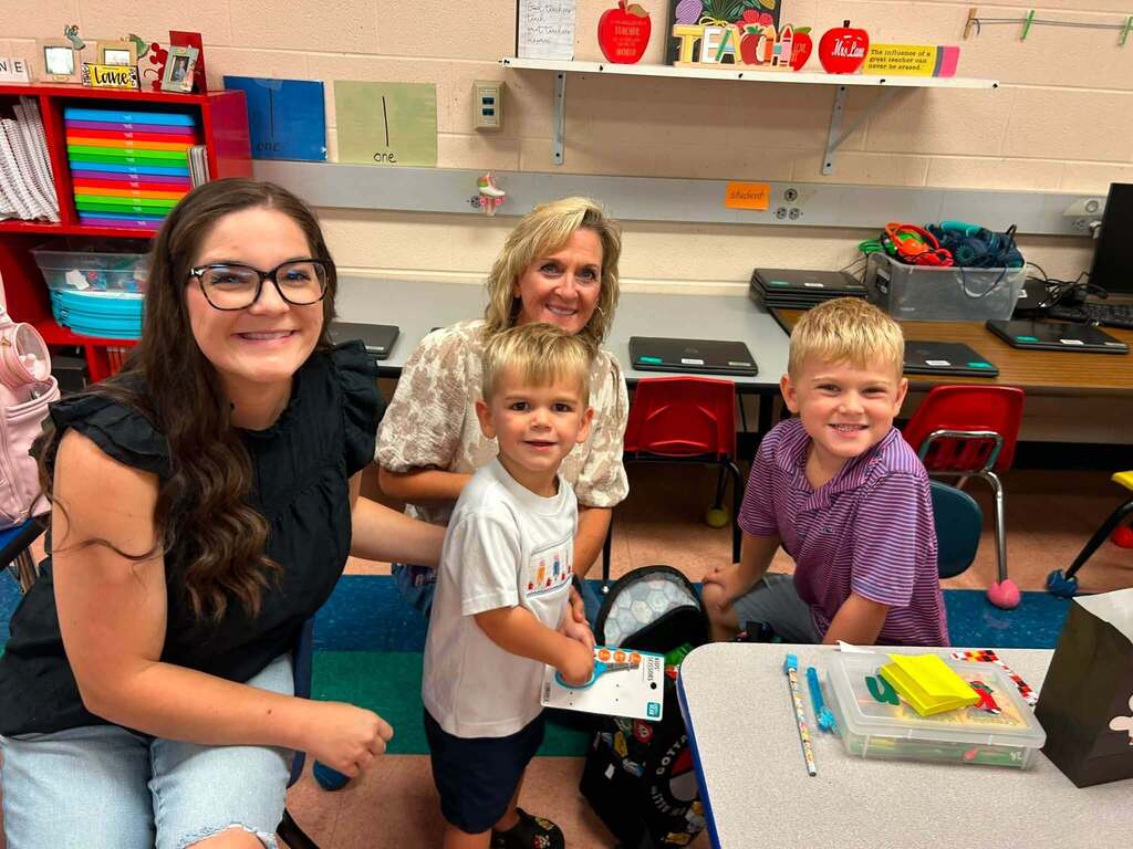 There are two adults and two children who are all sitting in chairs near a table in classroom.