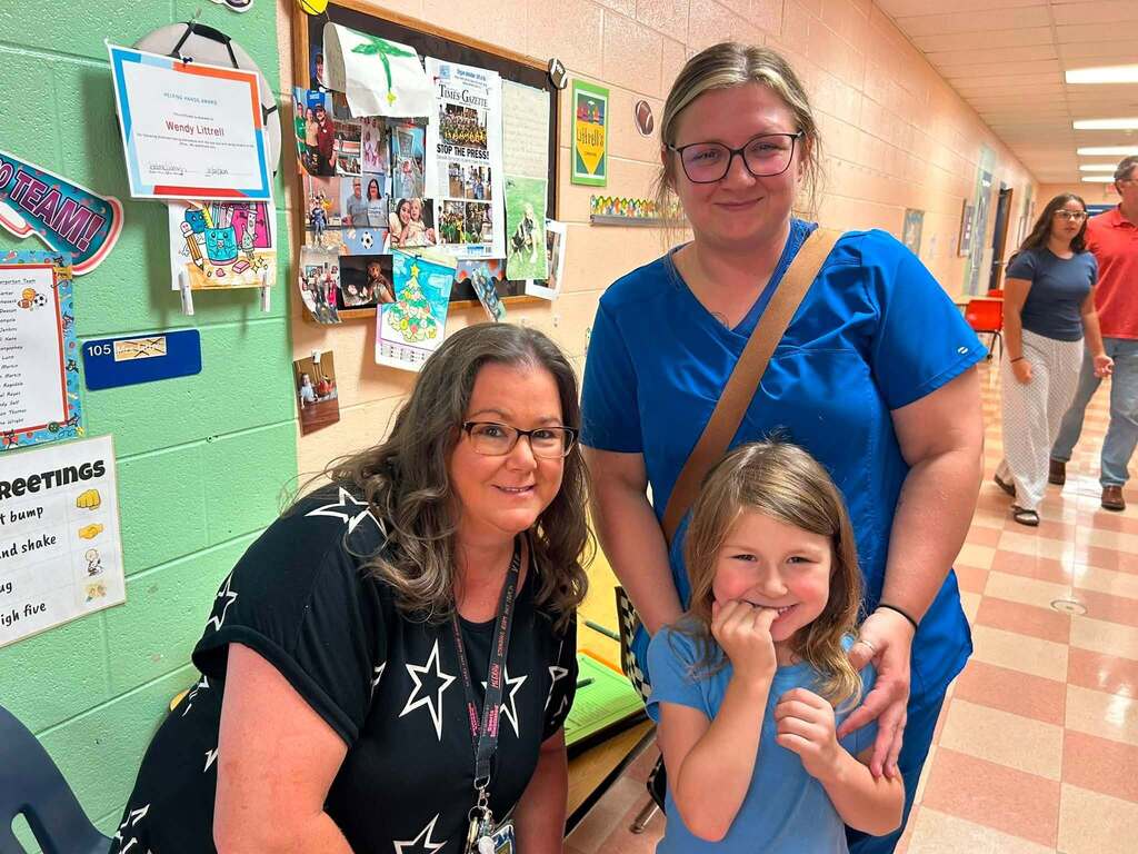 There are three people in this picture who are all posed for a group picture in the hallway of the school.