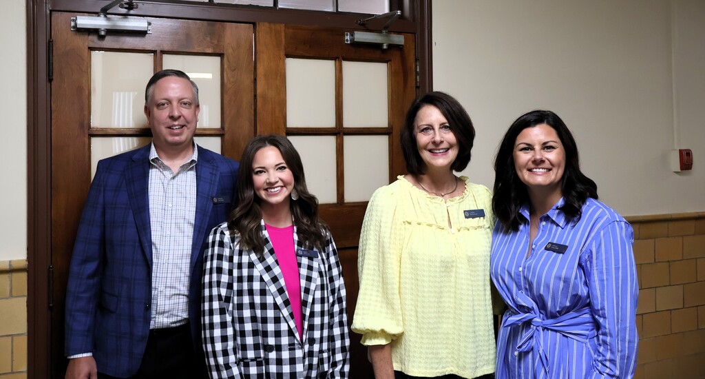 There are four people who are all posed for a group picture in the hallway. 