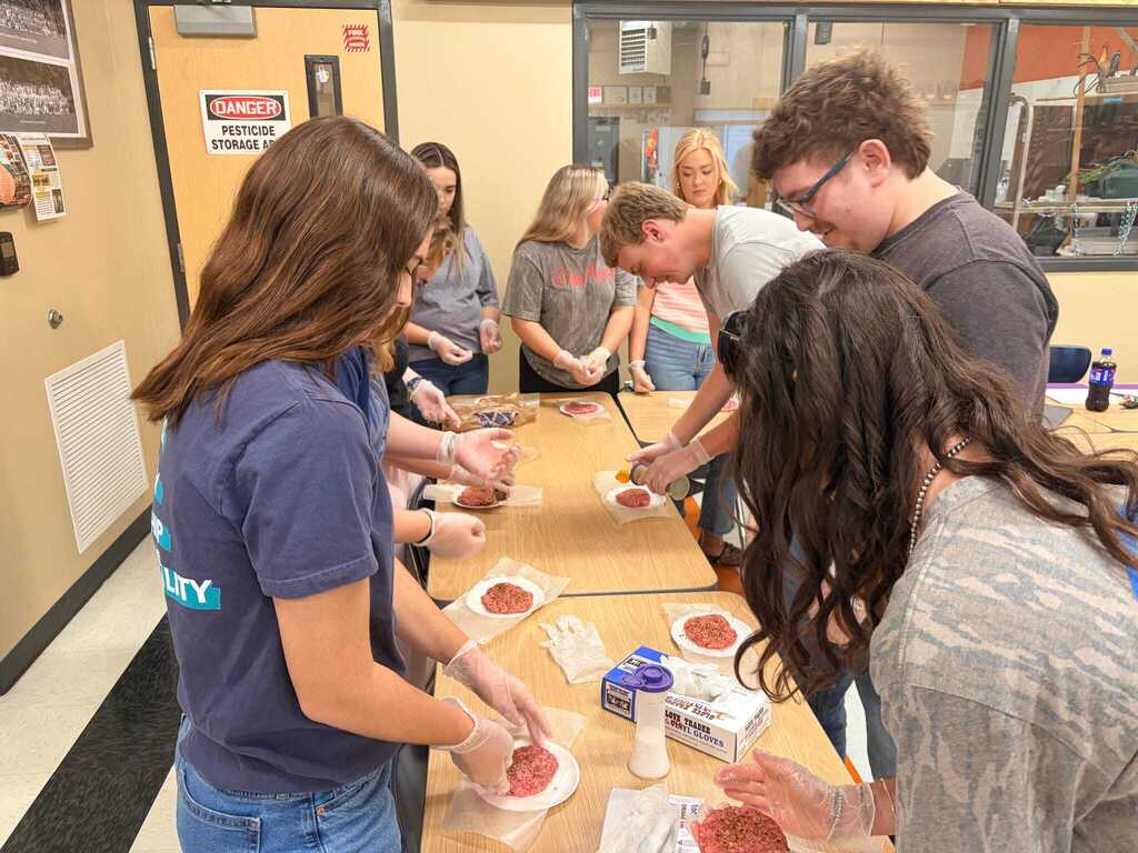 Group of veterinary science students wearing gloves examining formed meat patties on plates during hands-on class activity at Cascade High School.