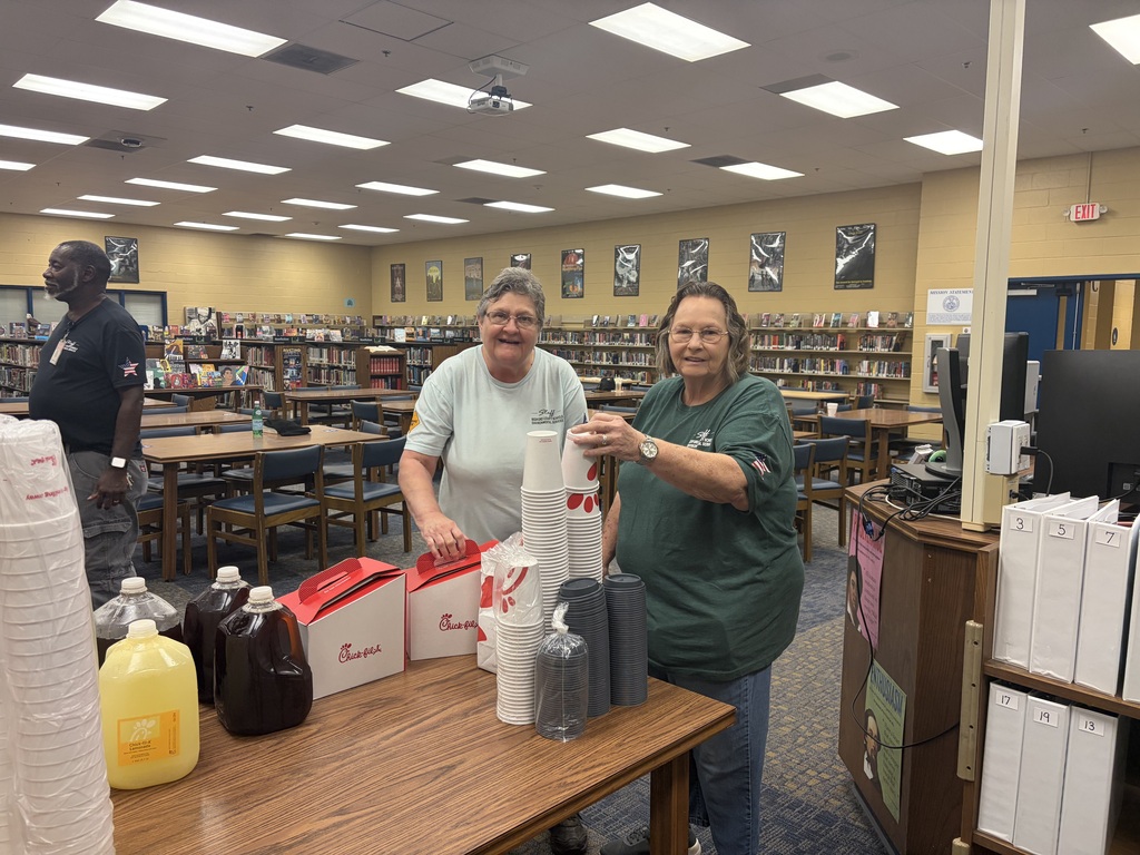There are two women standing in the library about to pour coffee into cups from Chic-fil-A.