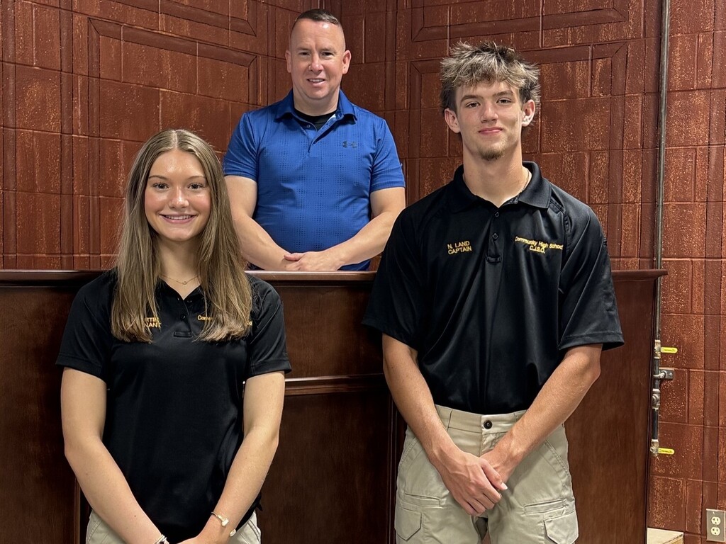 Two students along with their teacher are all posed for a group picture inside of their school's mock courtroom.