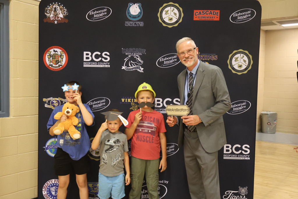There are three children in this photo each holding up a funny photo prop along withe superintendent who is also holding up one. 