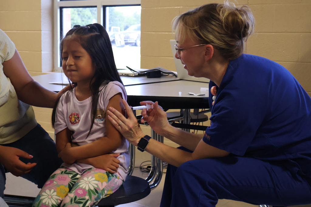There is a child in the photo who is getting a shot from a nurse.