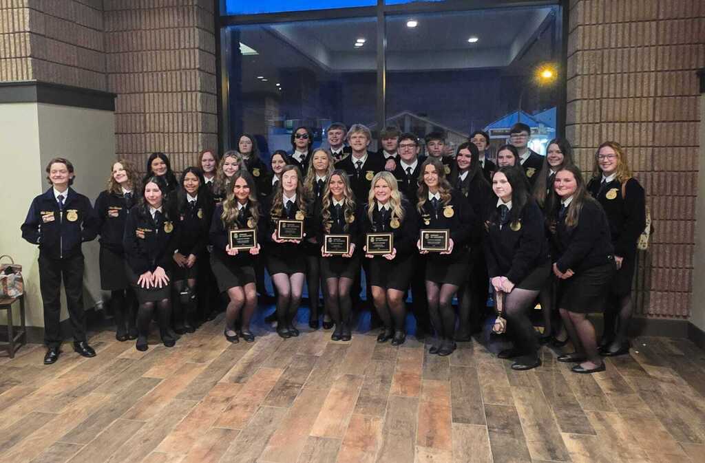 This is a group picture of FFA students who are all posed for a picture inside of a building and some of the students in the front are holding up plaques.