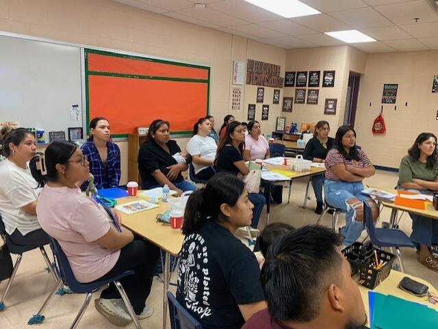 This is a picture of a classroom where several families are sitting at tables.