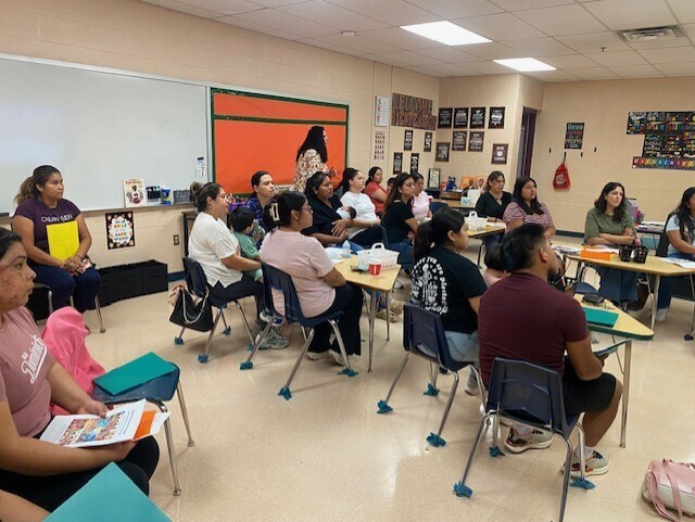 This is a picture of a classroom where several families are sitting at tables.