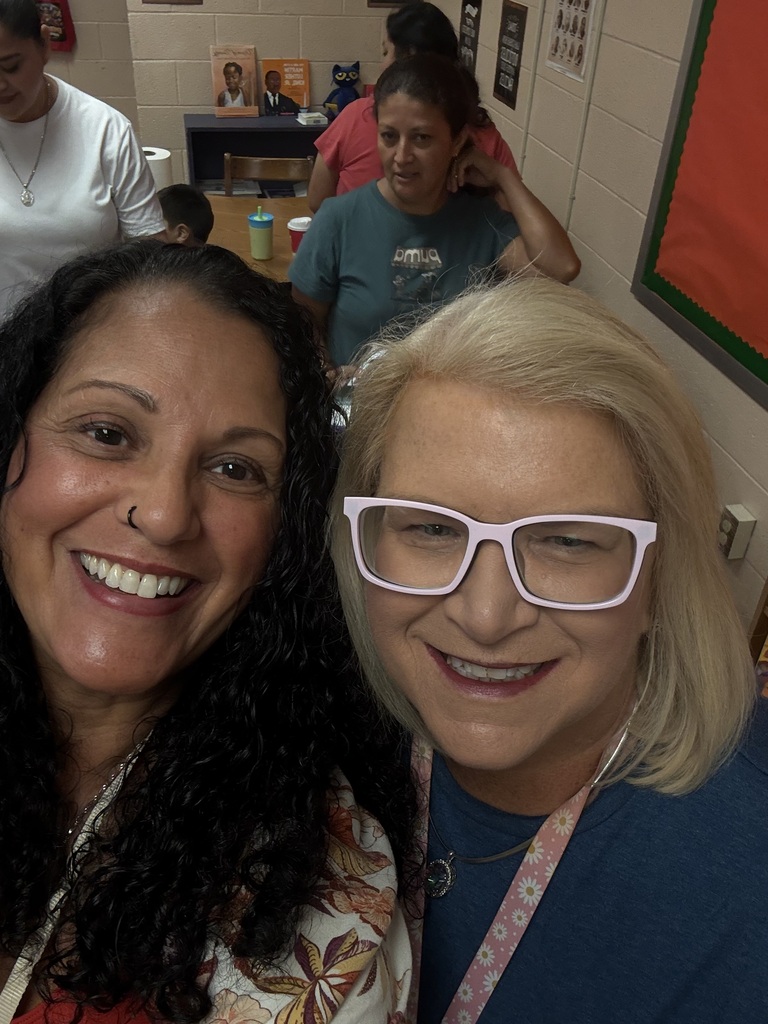 There are two females posed for a picture with three other people in the background behind them.