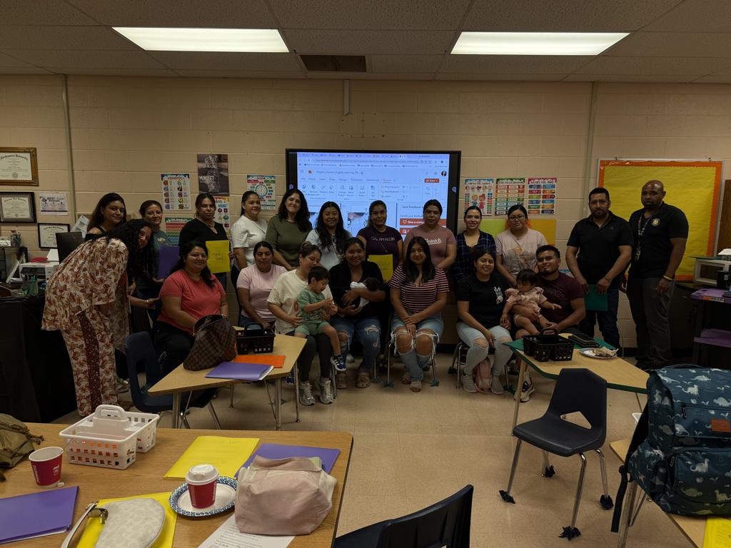 There are several people posed for a large group picture inside of a classroom all in front of a screen.