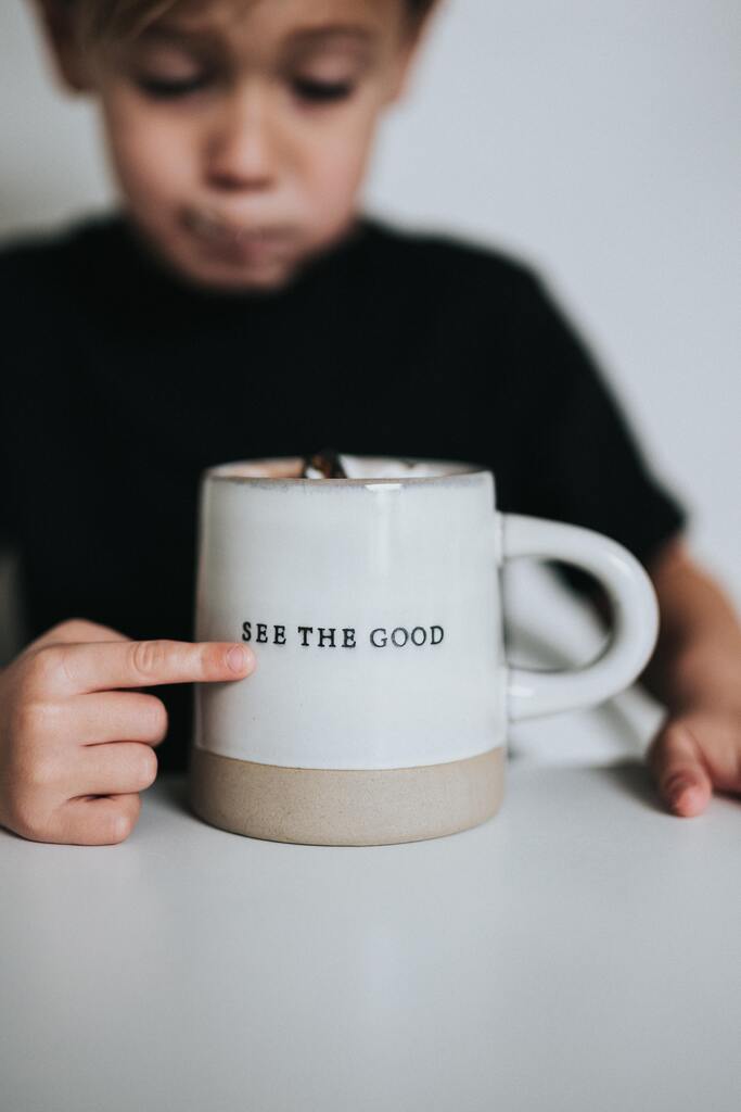 There is a little boy who is pointing to a coffee cup that says "SEE THE GOOD".