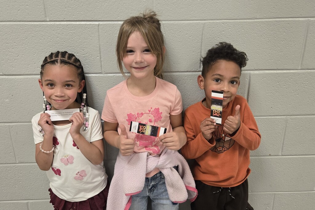 There are three students posed for a picture in the hallway and each are holding up a ticket to the Celebration. 