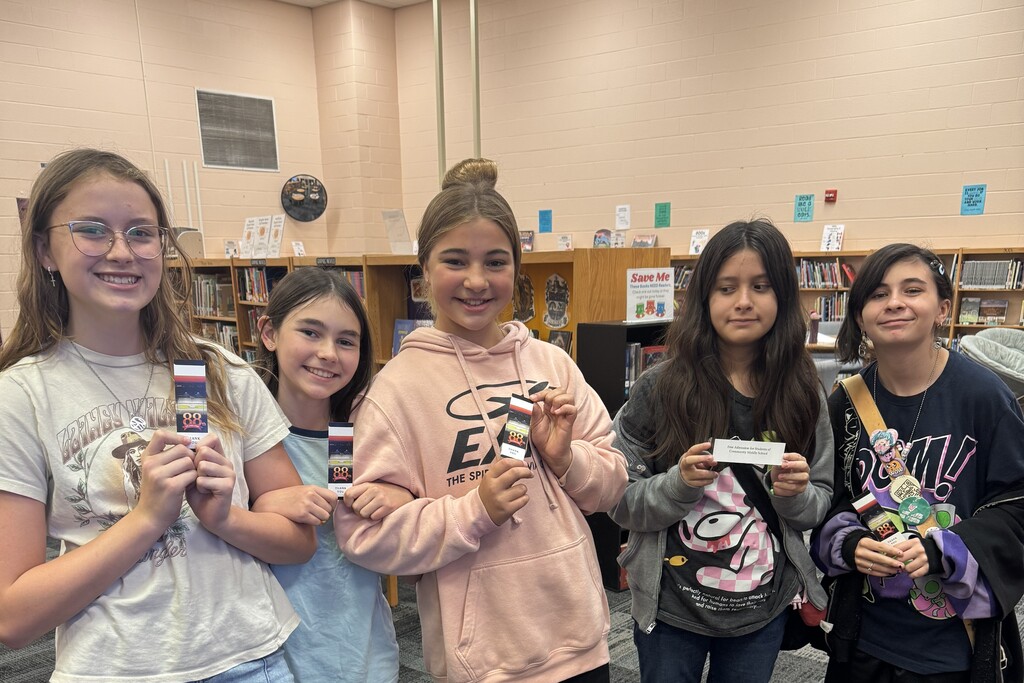 There are several students posed for a picture inside of the library and each are holding up a ticket to the Celebration. 