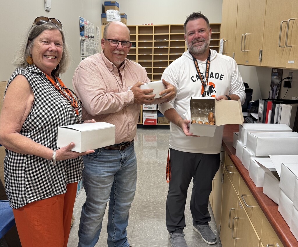 Three smiling staff members holding white donut boxes donated by Meghan Brainard and Eddie Burris from the horse show.