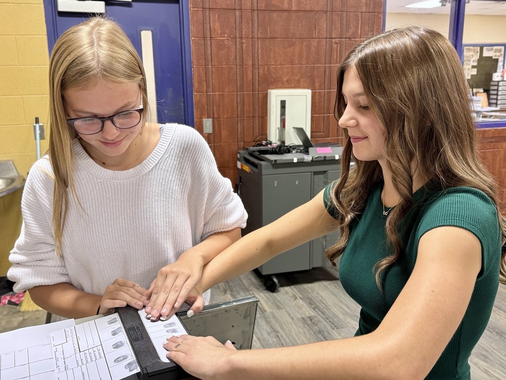 Two girls are standing inside a classroom practicing fingerprint application.