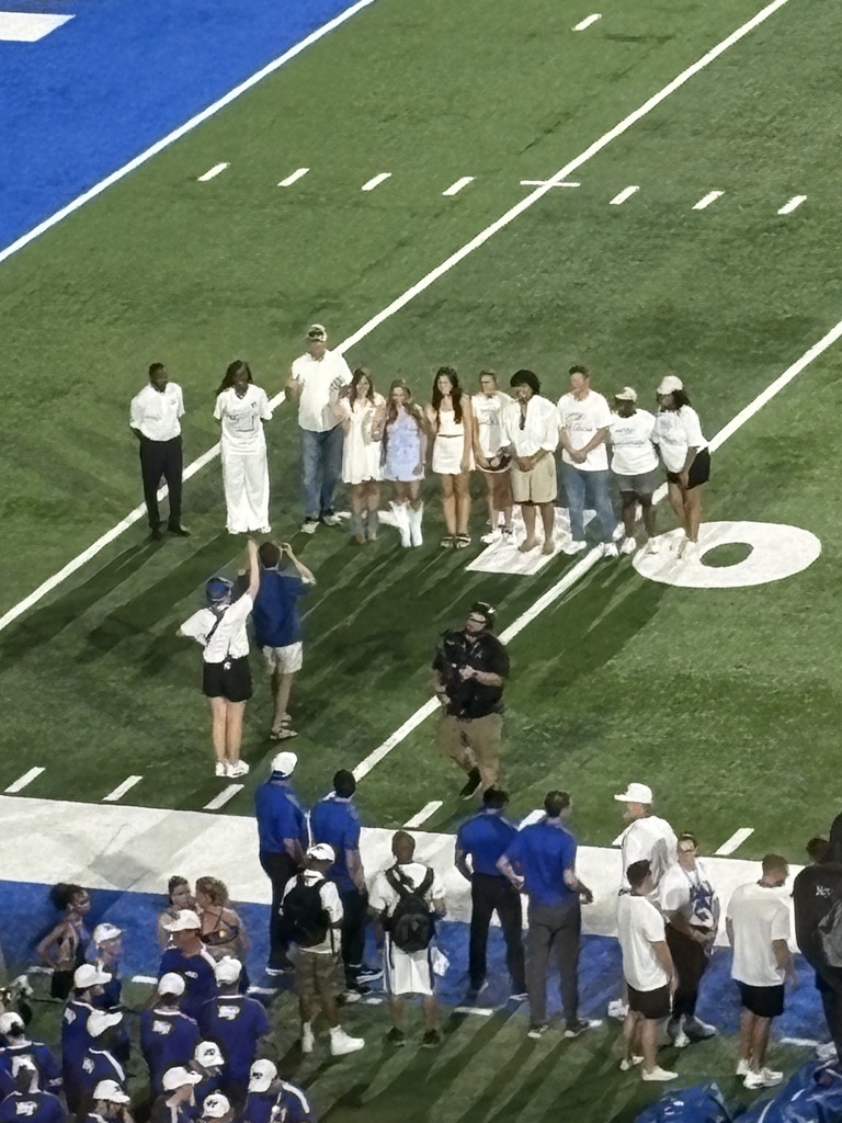 This is a picture from far away of the Teach Back Program Students along with several others who are all posing for a group picture on the football field at MTSU.