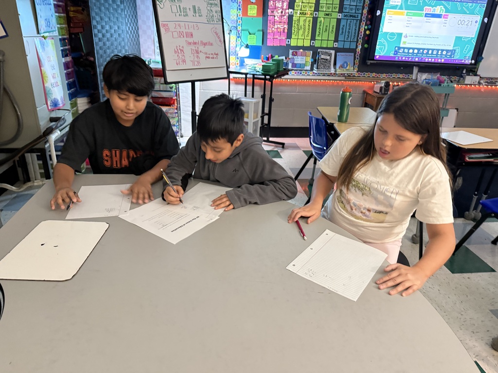 There are three students sitting at a table all working on math problems in their classroom.