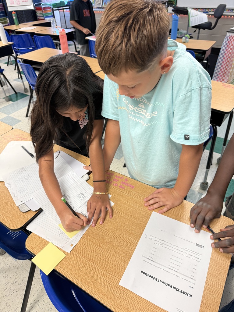 There are several students standing at their desks all working on math problems in their classroom.