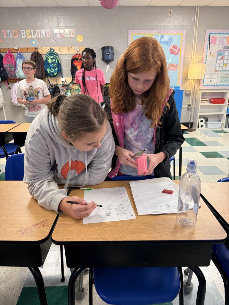 There are several students standing at their desks all working on math problems in their classroom.