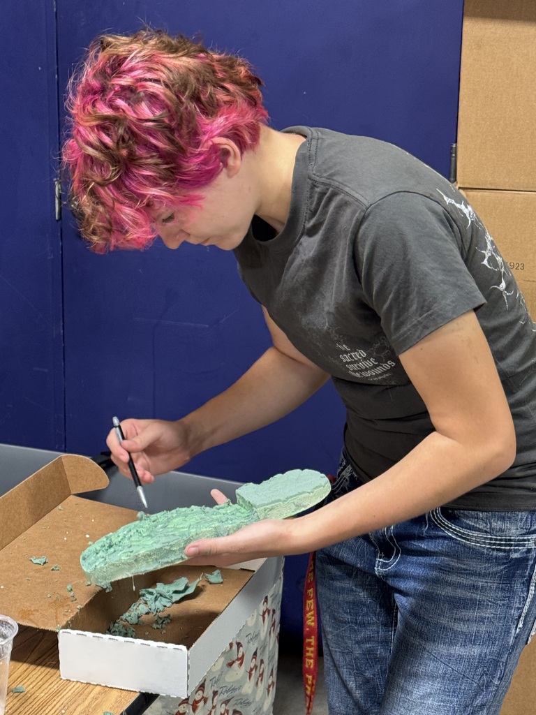 A student is standing in a classroom at a table making a cast of a shoe that they are holding. 