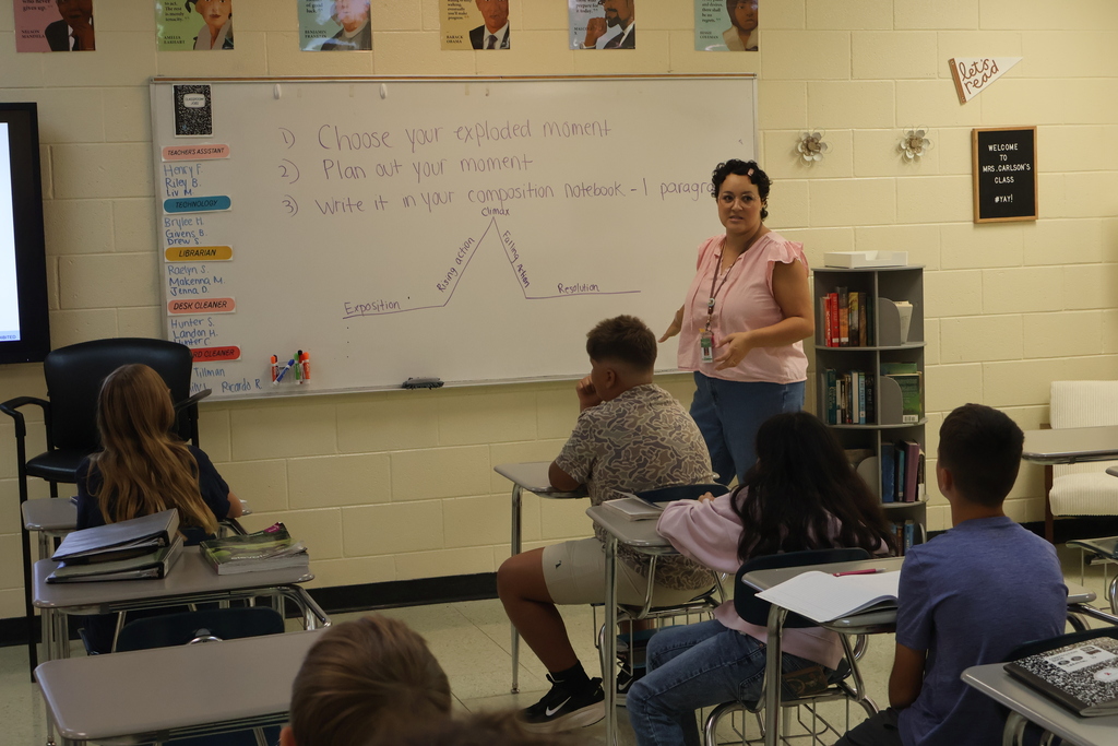 A teacher is standing before her class asking them questions that she has put down on the white board. 
