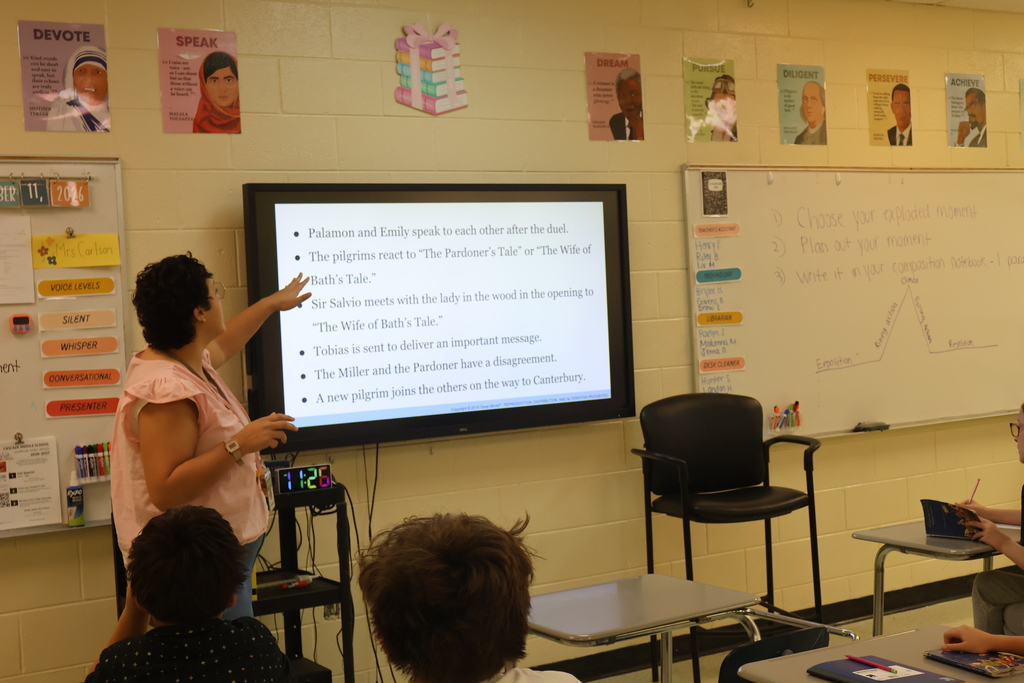 A teacher is standing before her class asking them questions that she has put down on the white board. 