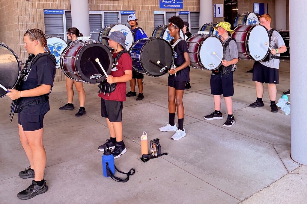 There are several students holding their drums in a row outside.