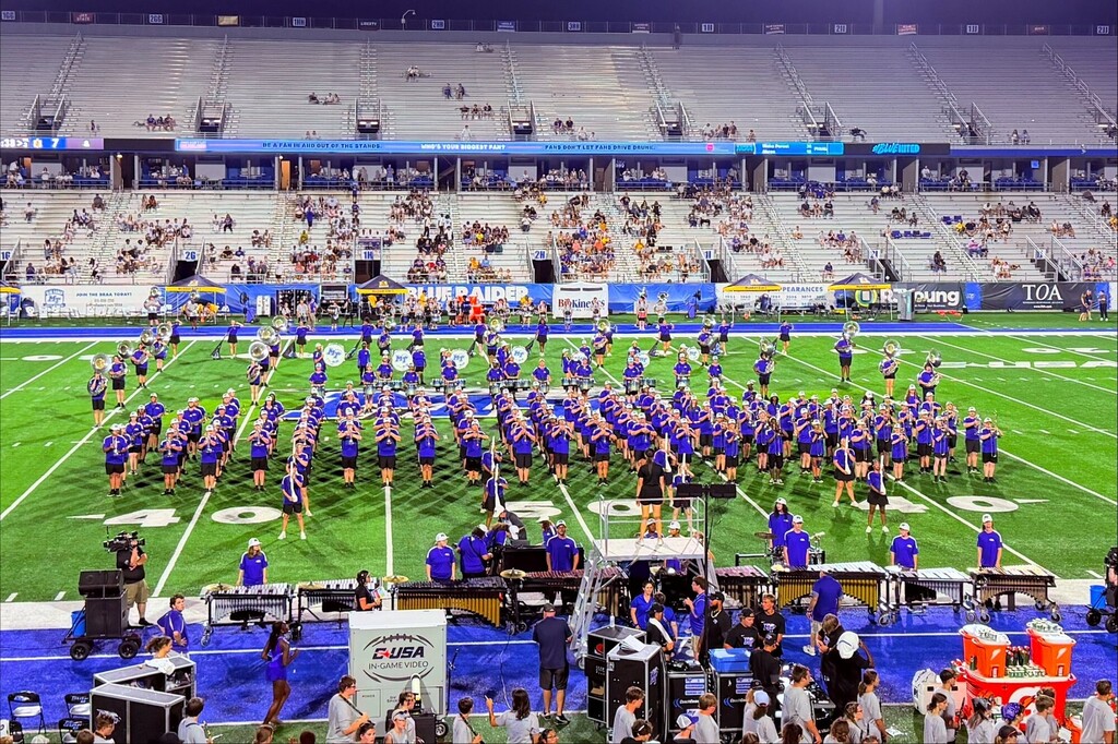 The band of MTSU and SCHS are all gathered together in a large group playing musical instruments during their performance.