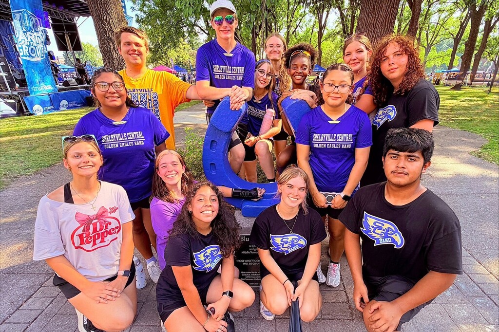 There are several students all posed for a group picture outside on the MTSU campus by the blue horseshoe.