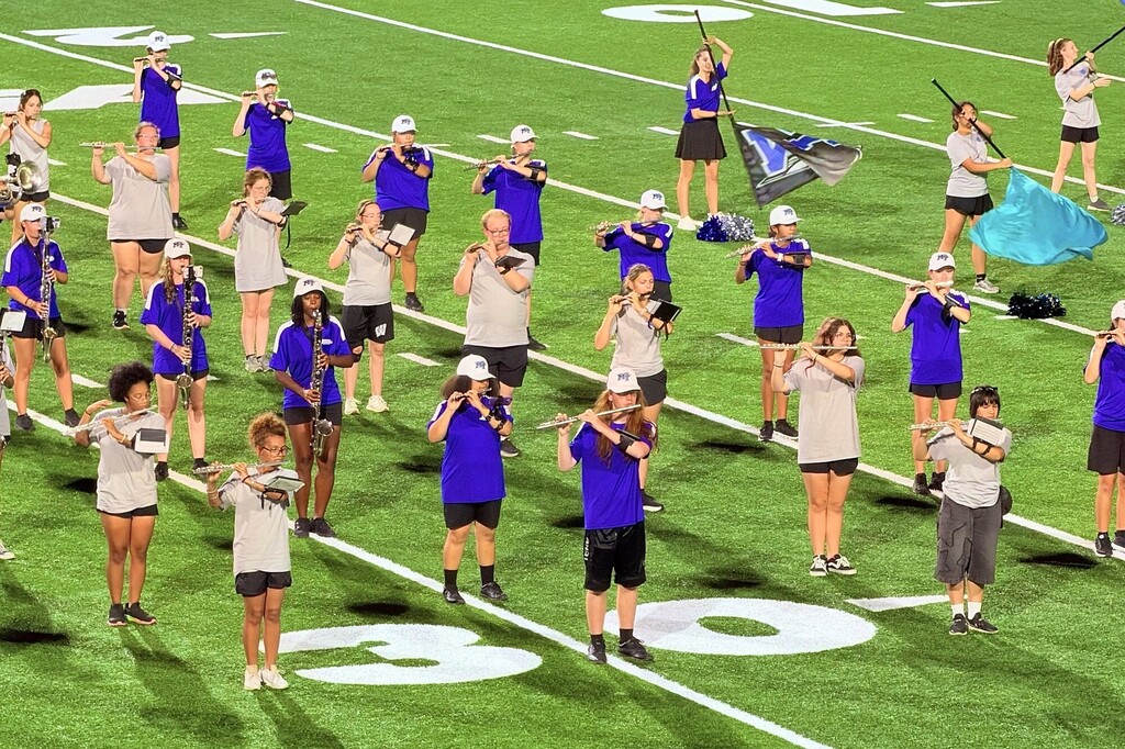 There are band members on the football field at MTSU all in a line while playing their musical instruments during their performance.