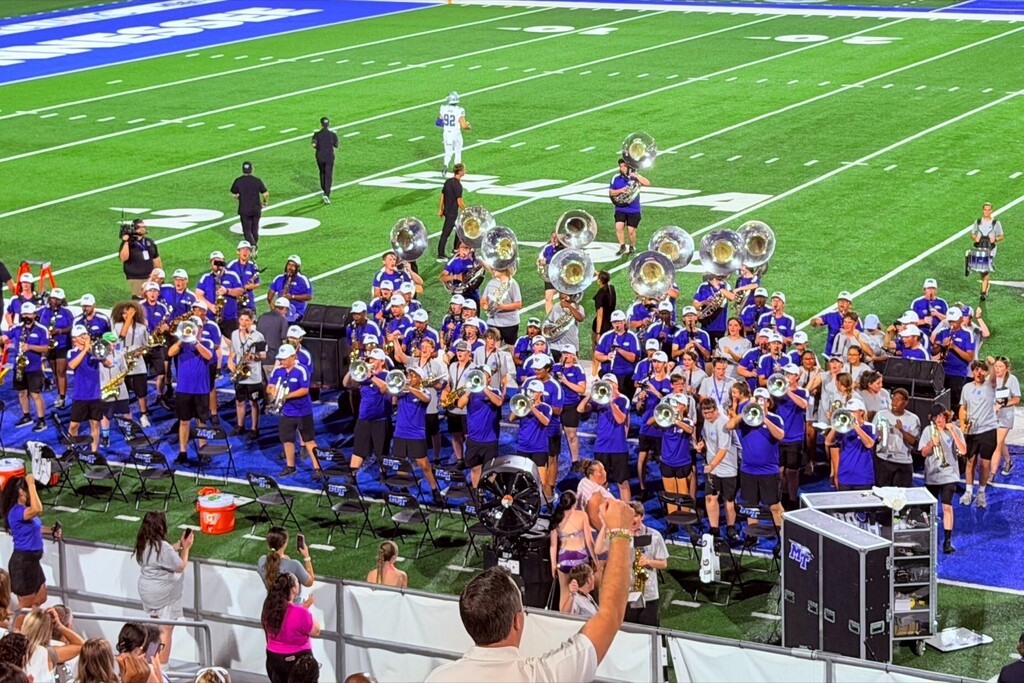 The band of MTSU and SCHS are all gathered together in a large group playing musical instruments during their performance.