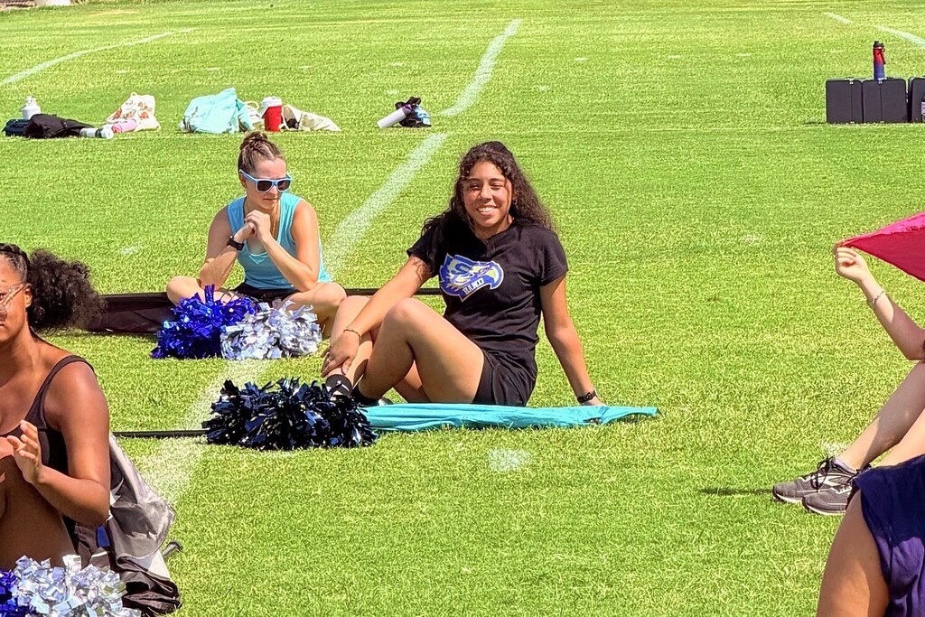 A student is sitting outside on a football field with pom poms and a flag.