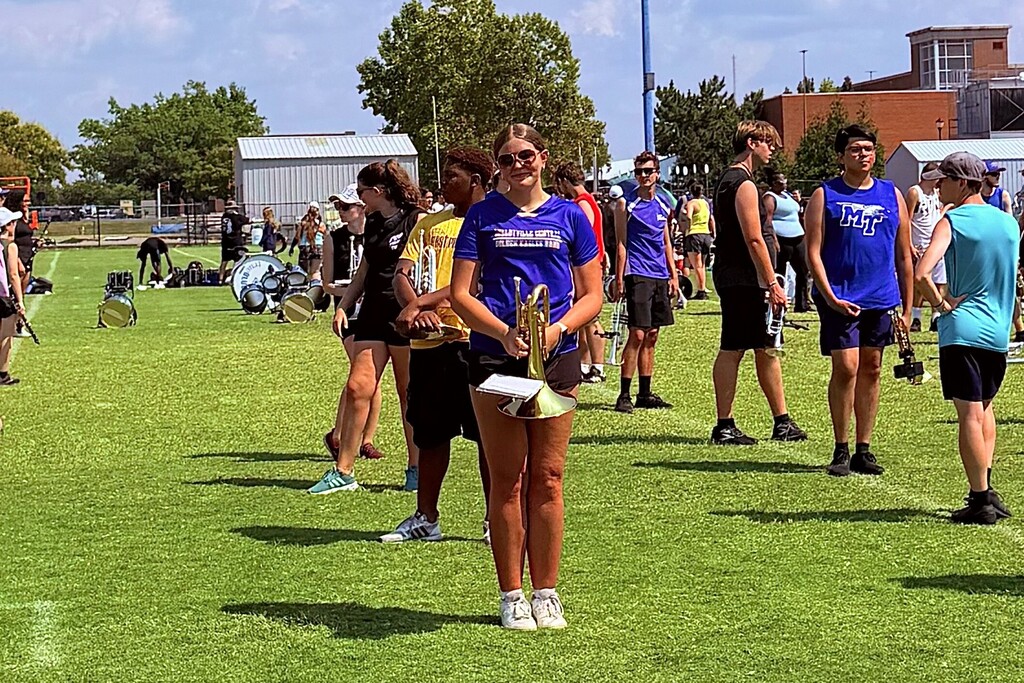 This is a picture of a student on a field holding her musical instrument with several others in the background doing the same.