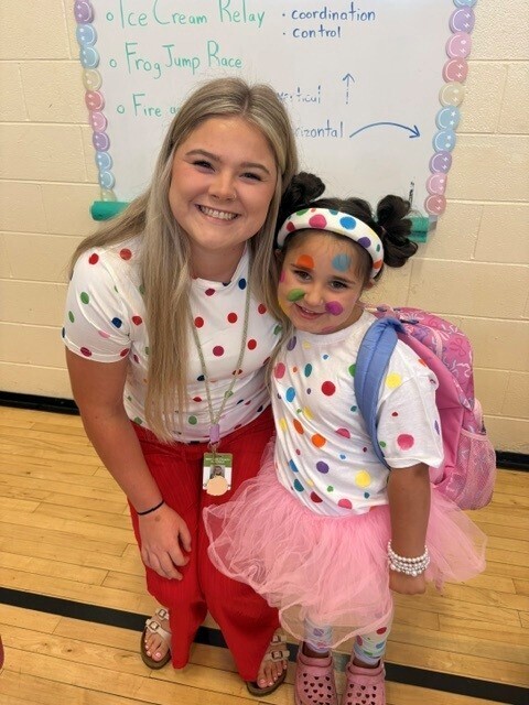 A teacher and student are both posed for a picture while wearing a colorful dot outfit. 