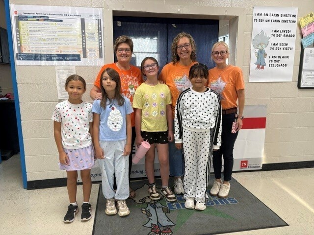 There are four students along with the admin team and a teacher who are all posed for a group picture in the hallway while wearing dots on their clothing. 