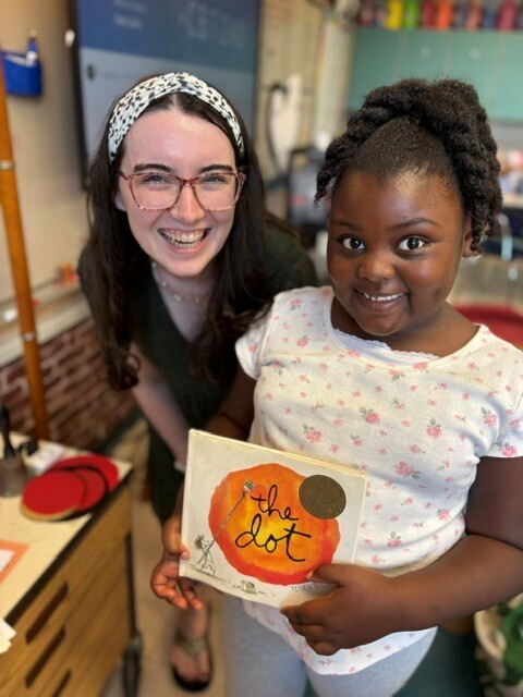 A teacher and a student are both posed for a picture while the student is holding the book "The Dot".