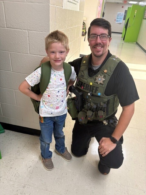 The SRO and a student are both posed for a picture in the hallway while wearing their colorful dots. 