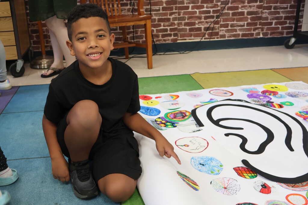 A student is pointing to the dot he decorated after it was added to the large sheet of paper. 