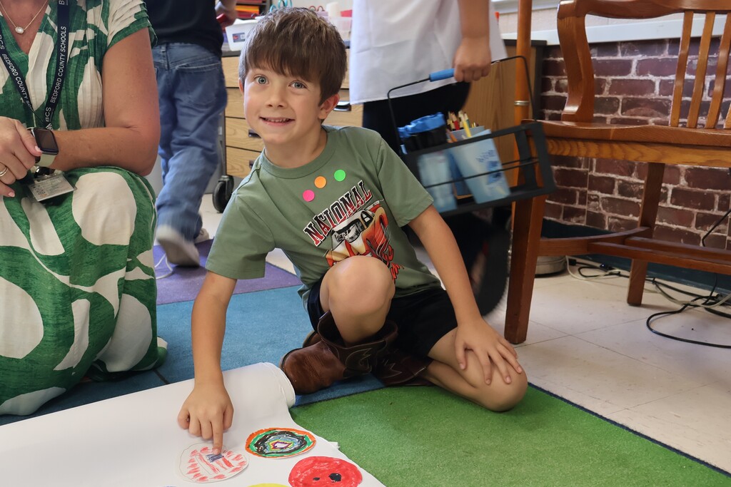 A student is pointing to the dot he decorated after it was added to the large sheet of paper. 