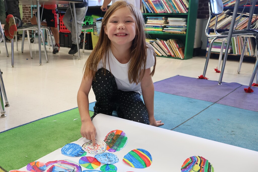 A student is pointing to the dot she decorated after it was added to the large sheet of paper. 
