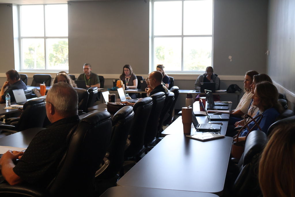 There are people seated at long tables with their laptops open. 