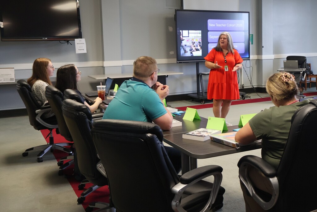 A person is speaking to the group who are all seated at tables in the staff development room. 