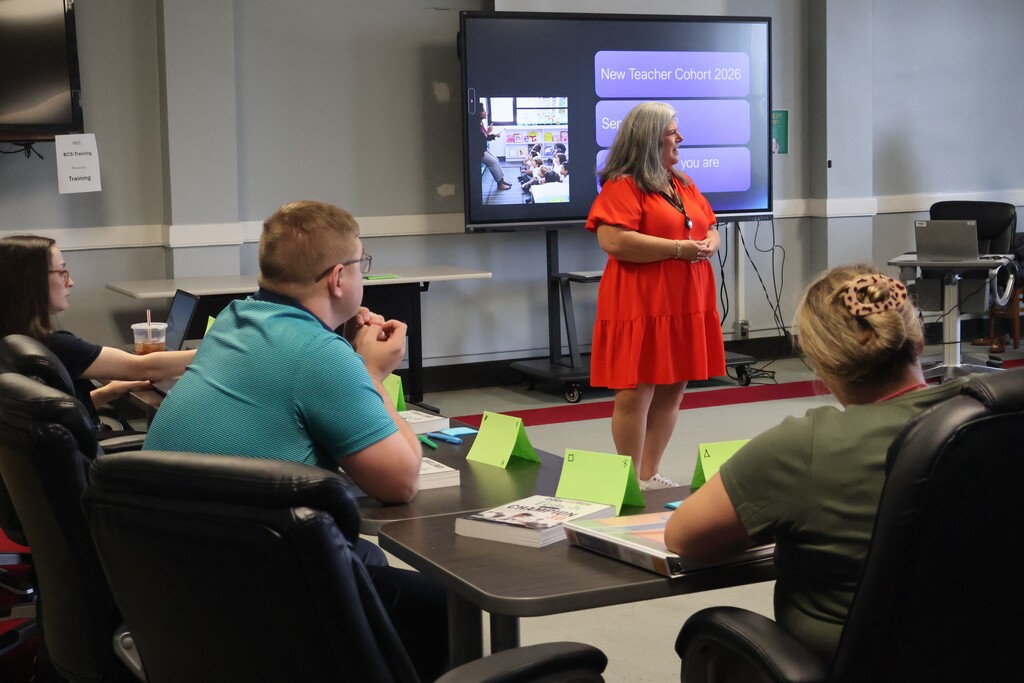 A person is speaking to the group who are all seated at tables in the staff development room. 
