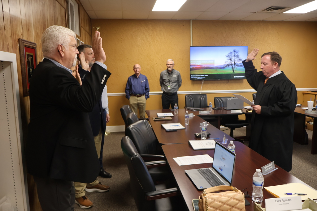 Four school board members are standing before a judge at the Central Office as they take their new Oath of Office for their new terms. The superintendent and another school board member are standing off to the side watching. 