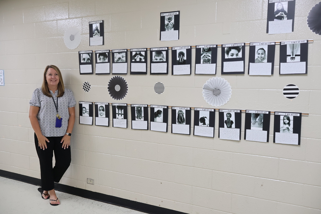 The teacher is posed for a picture in the hallway by the display of black and white photos. 