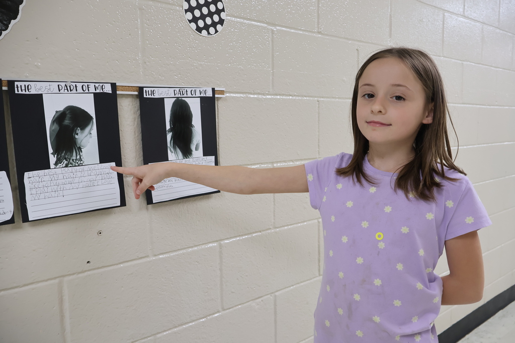 A girl points to the black and white picture she chose along with the writing she did underneath it. 
