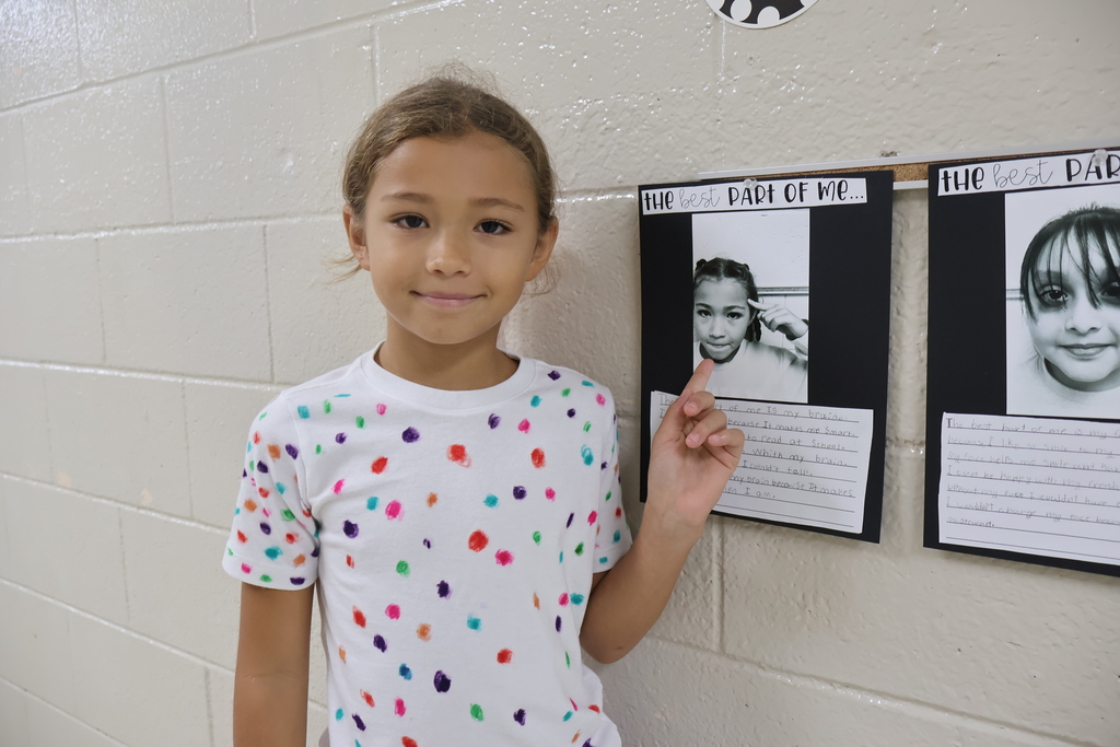 A girl points to the black and white picture she chose along with the writing she did underneath it. 